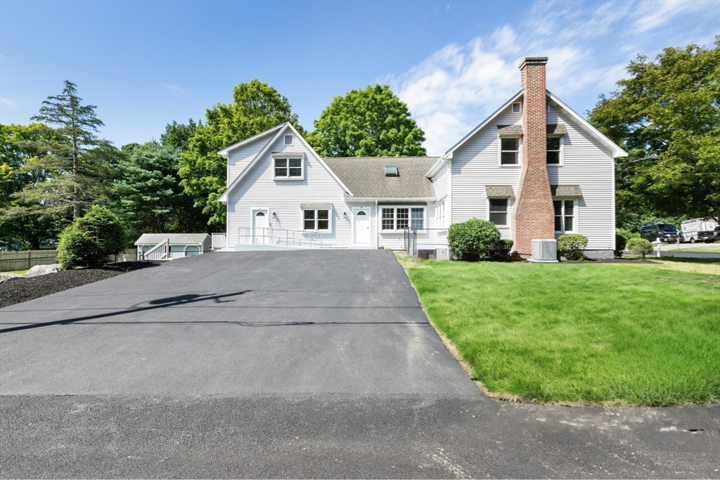White multi-gabled house with a brick chimney, broad driveway, and green lawn.