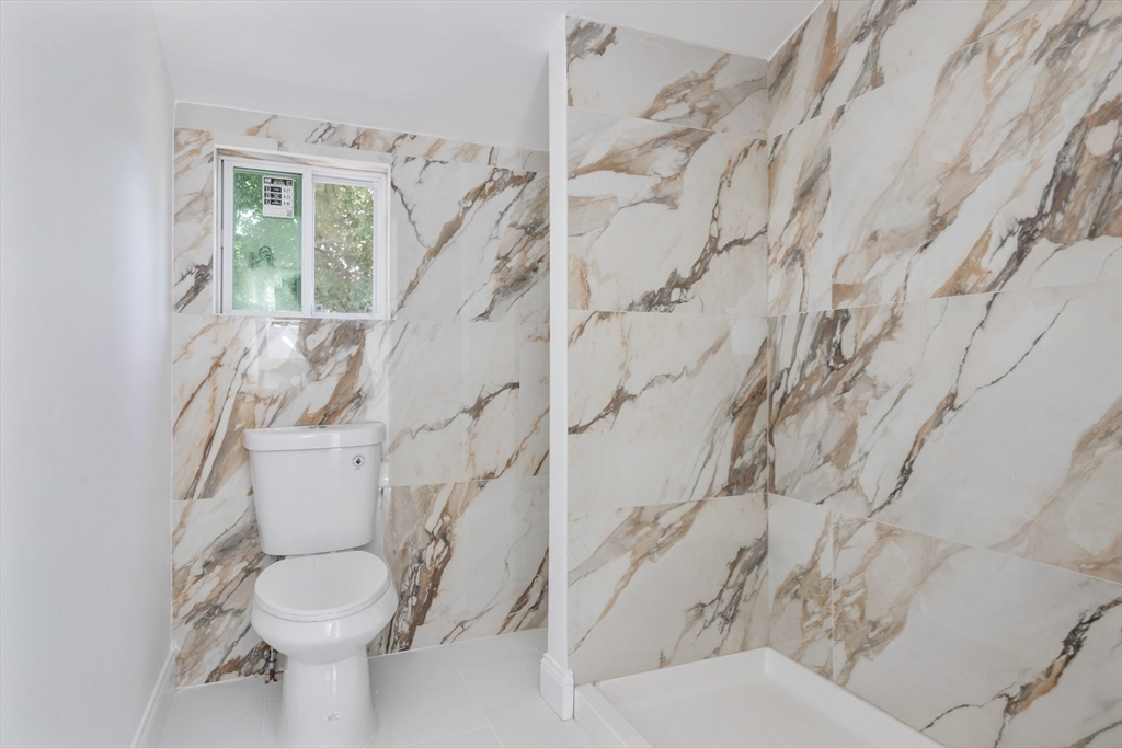 Bathroom with a toilet, marble-look shower walls, and a small window.