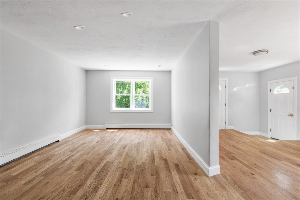 Vacant room with hardwood floors, a large window, and an adjoining entry area.
