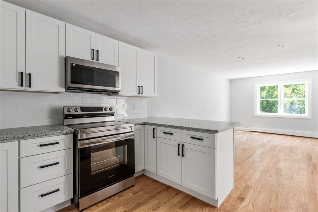 Kitchen with white cabinets, stainless steel appliances, granite counters, and hardwood floors.