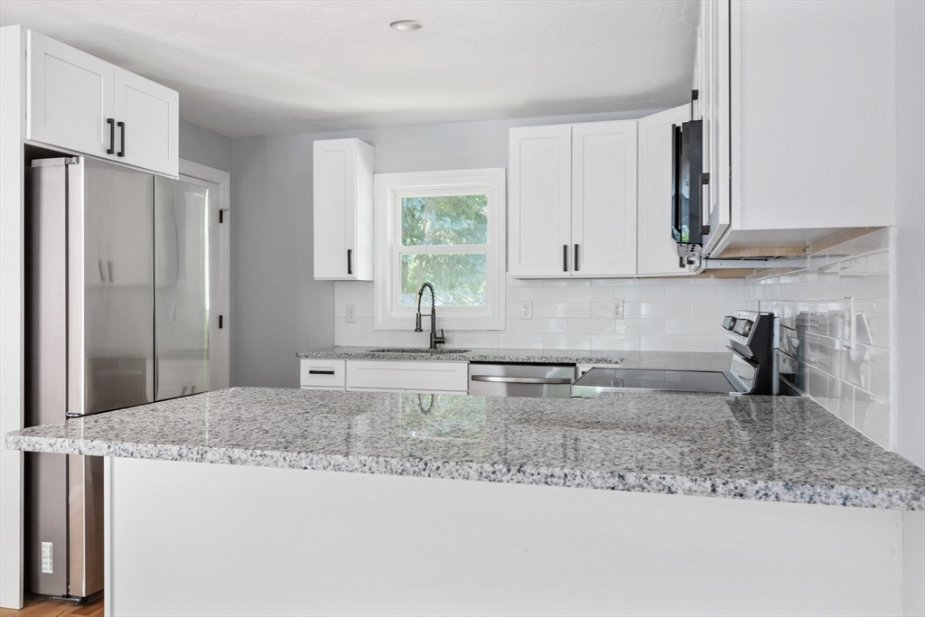 Kitchen with granite counters, white cabinets, stainless steel appliances, and a window above the sink.
