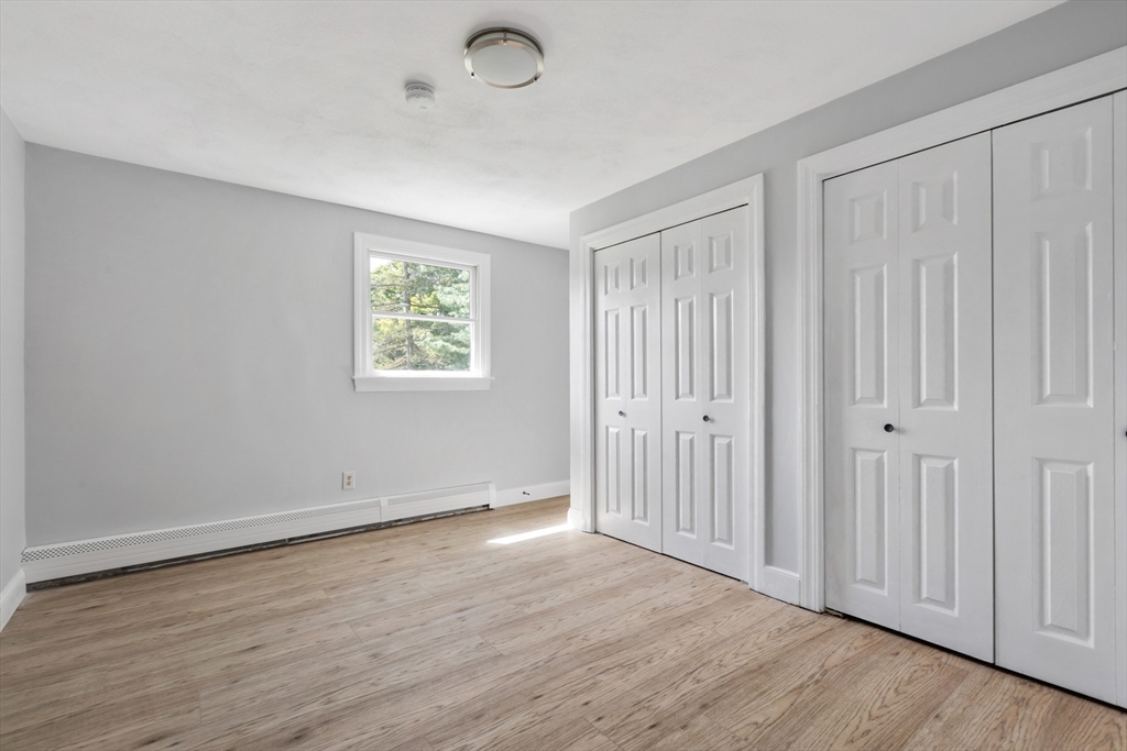Empty bedroom with light wood-look flooring, a small window, and two sets of closet doors.