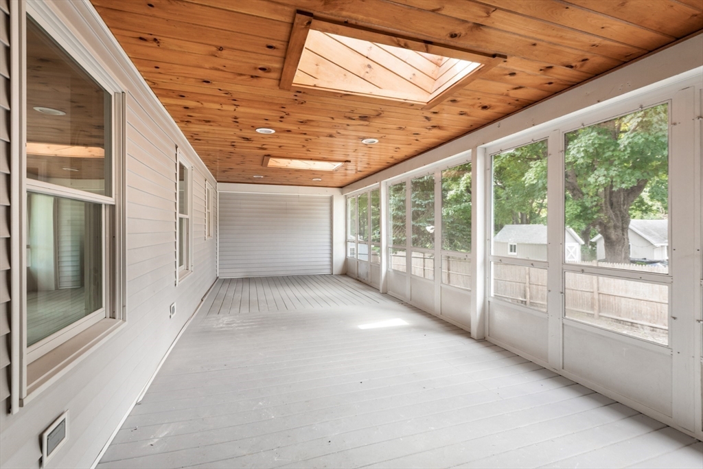Empty enclosed porch with white plank flooring, a wood ceiling, skylights, and large windows.