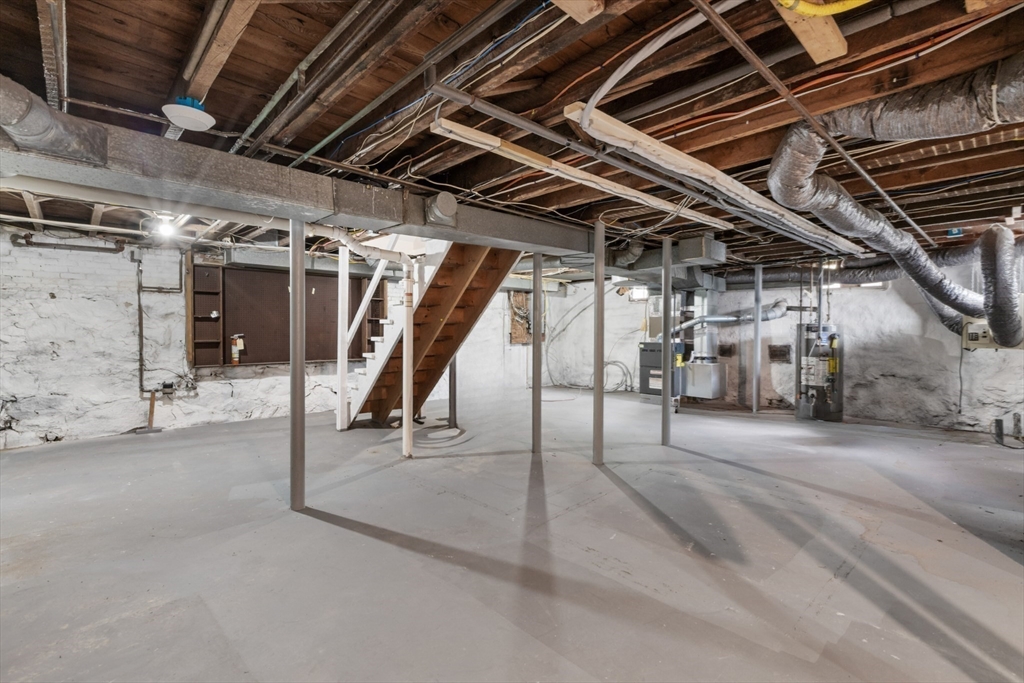 Unfinished basement with exposed ceiling joists, support posts, concrete floor, and visible mechanical equipment.