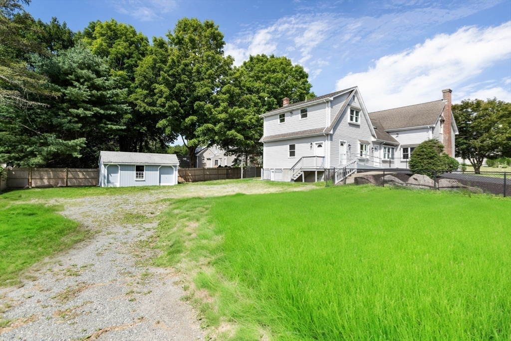 White two-story house with a raised deck, small shed, gravel drive, and broad lawn.