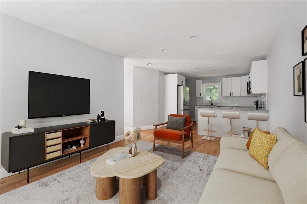 Open-plan living room and kitchen with a cream sofa, orange chair, and white island with three stools.