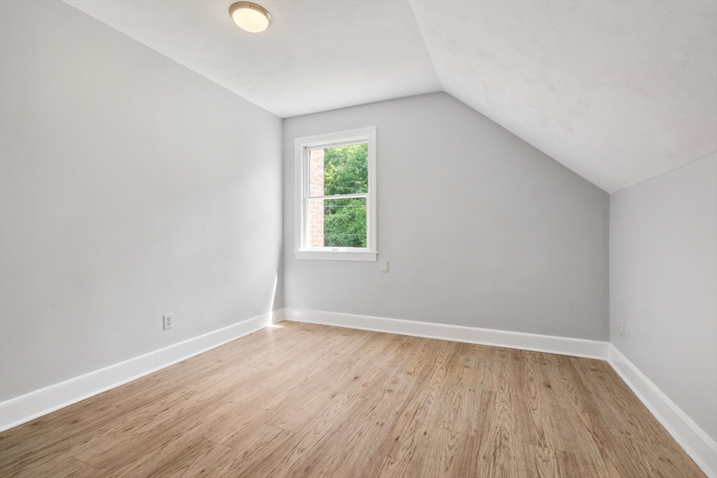 Vacant finished room with light wood flooring, a sloped ceiling, and a single window.