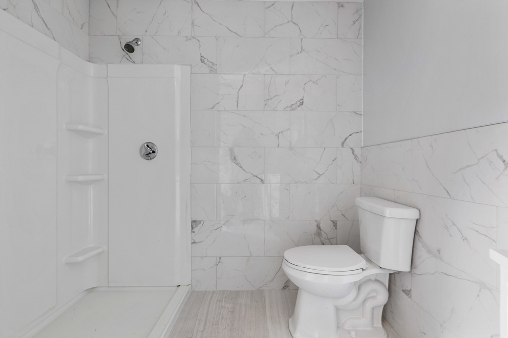 Bathroom with a marble-look tiled shower, built-in shelves, toilet, and light wood-look flooring.