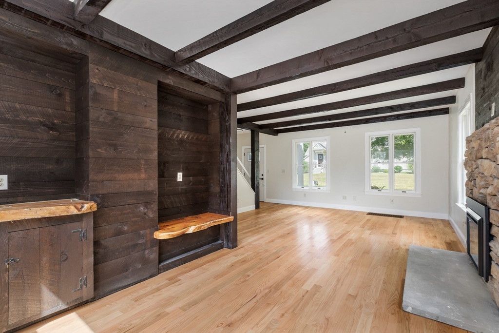 Living room with exposed dark beams, hardwood floors, built-in seating, and a stone fireplace.