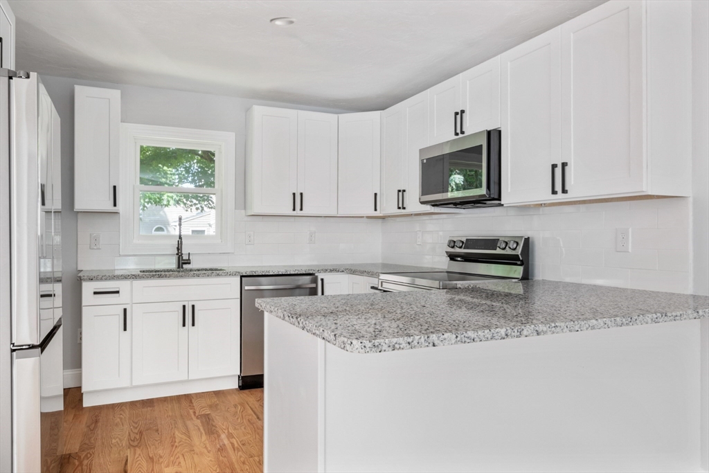 Kitchen with white cabinets, granite island, stainless steel appliances, and hardwood floors.