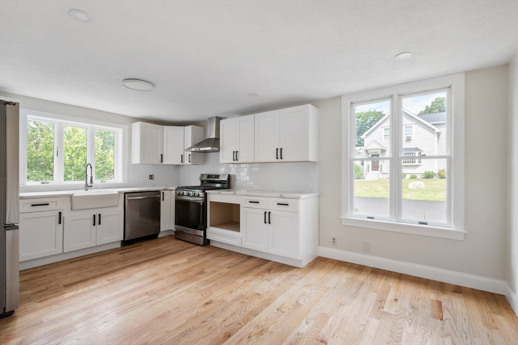 Empty kitchen with white cabinets, stainless steel appliances, and light wood floors.