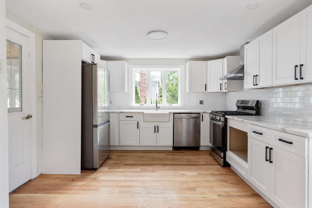 Bright white kitchen with stainless steel appliances, farmhouse sink, subway tile backsplash, and hardwood floors.