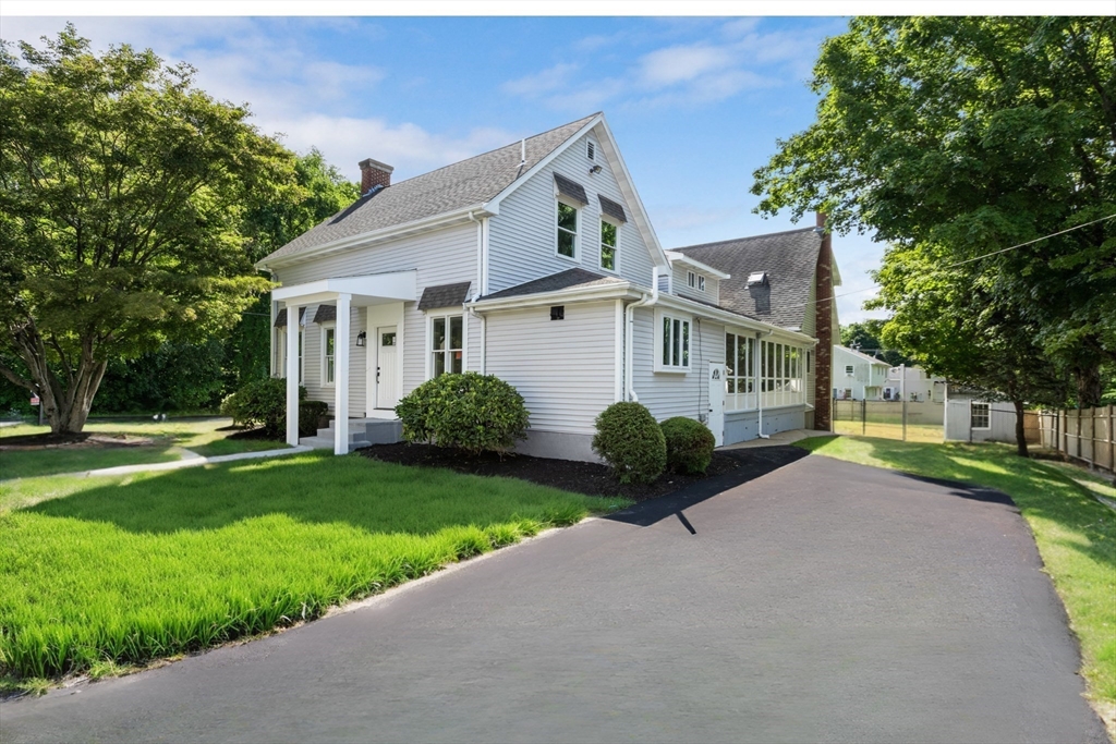 White-sided house with a covered entry, broad paved driveway, and leafy lawn.