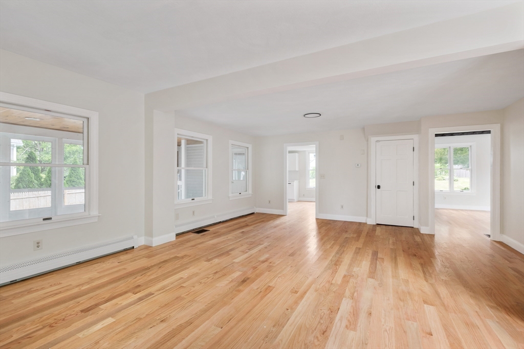 Vacant living area with hardwood floors, multiple windows, and open adjoining rooms.