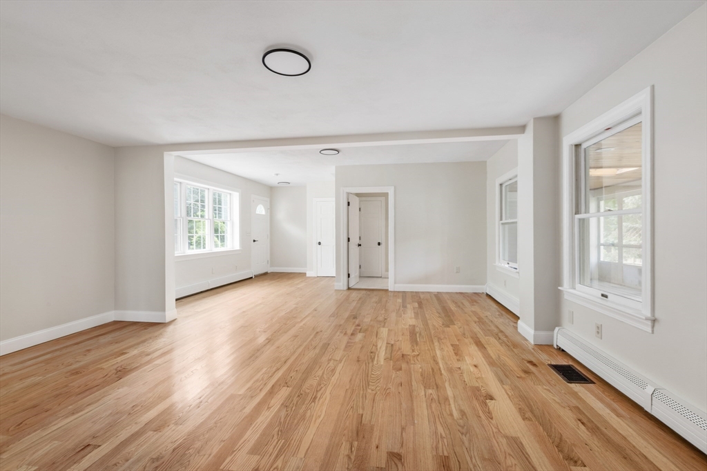 Empty living room with light hardwood floors, large windows, and an open adjoining area.