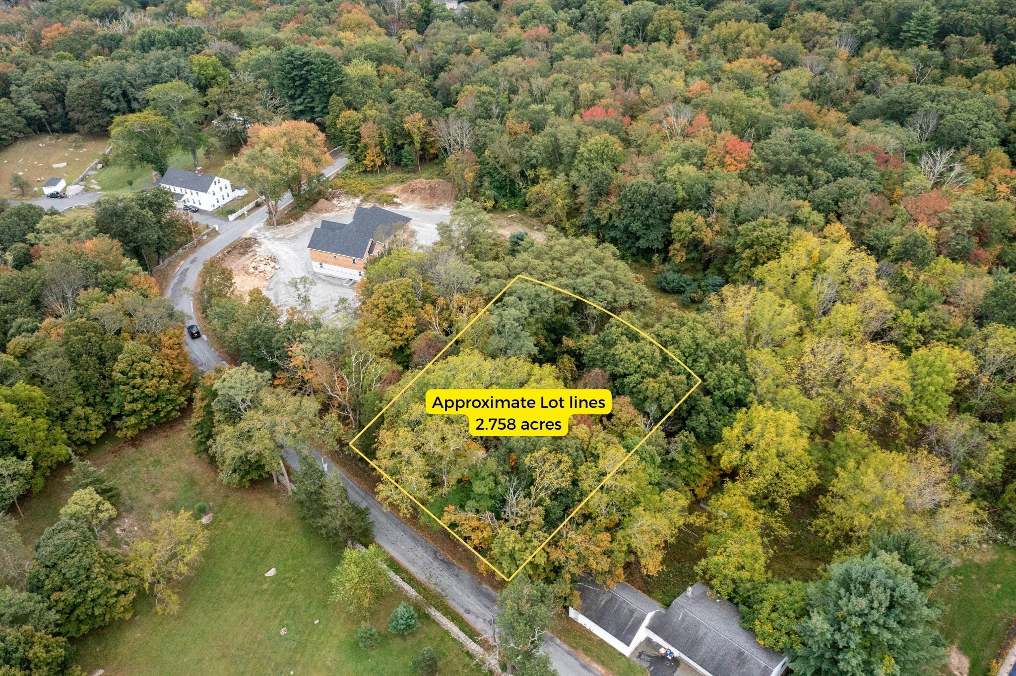 Aerial view of a wooded 2.758-acre lot outlined in yellow beside a rural road.