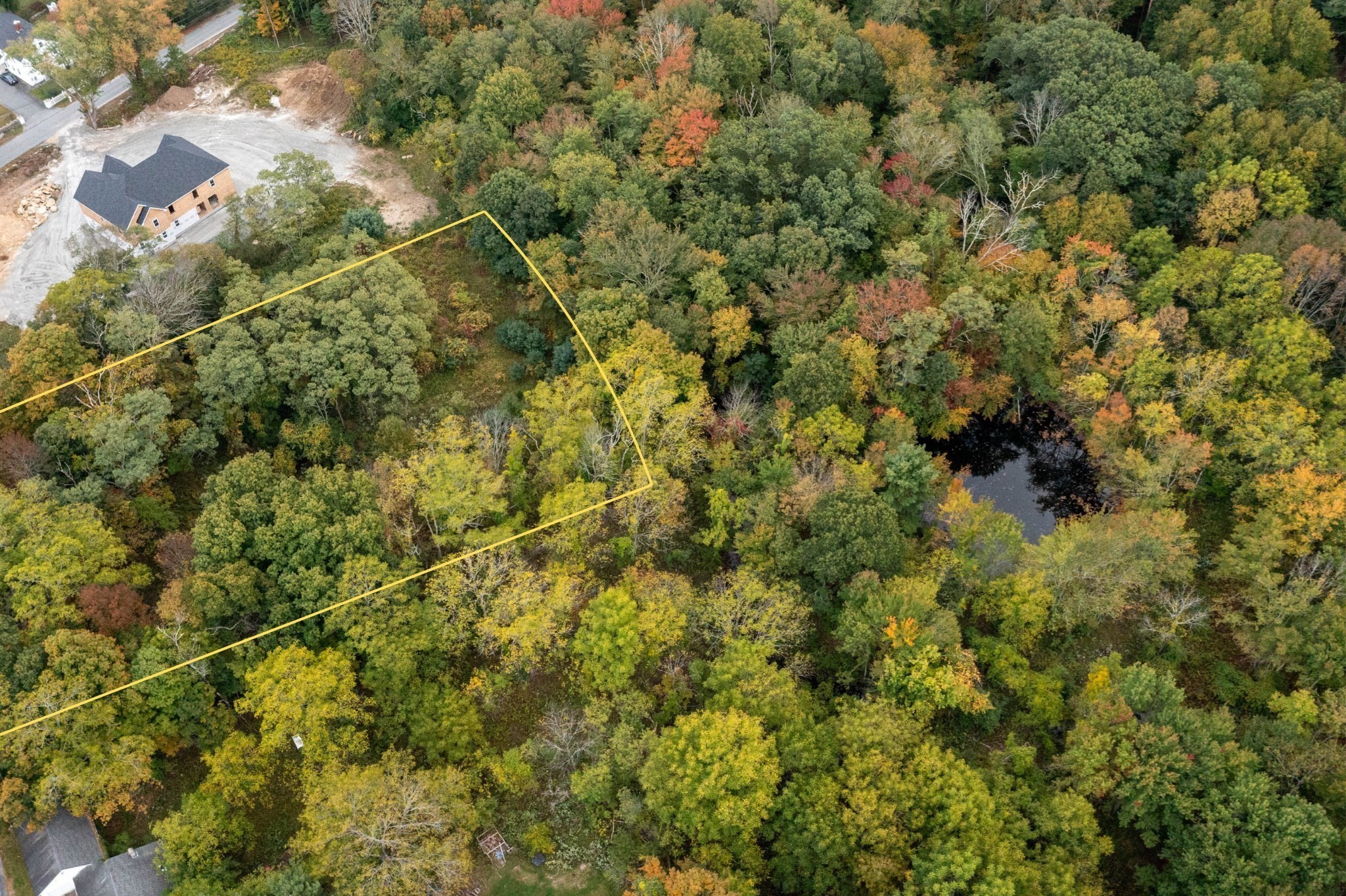 Wooded lot outlined in yellow, with a nearby pond and new home.