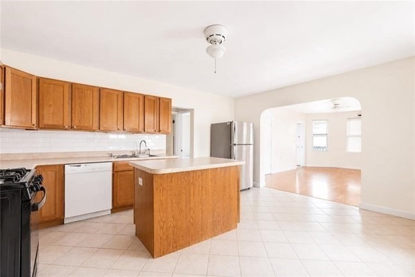 Kitchen with wood cabinets and a central island opening to a bright adjoining room.