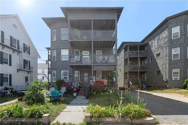 Gray three-story residential building with stacked porches and a landscaped front yard.