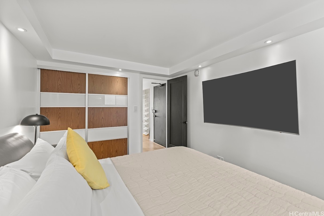 Bedroom with a white bed, wood-paneled sliding closet doors, and a large wall-mounted television.