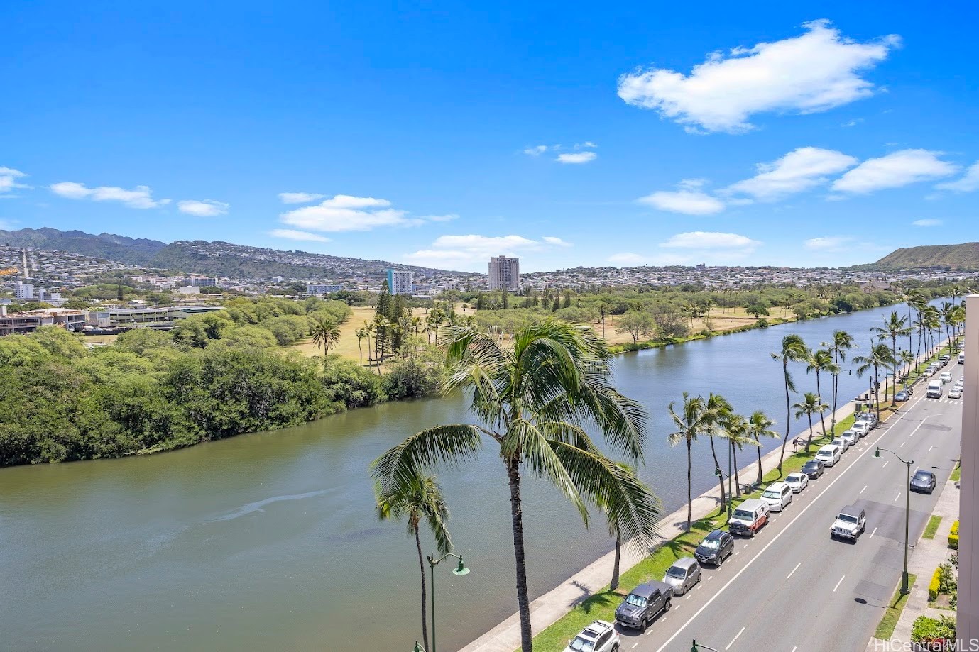 View over the Ala Wai Canal, palm-lined boulevard, and Honolulu neighborhoods toward the hills.