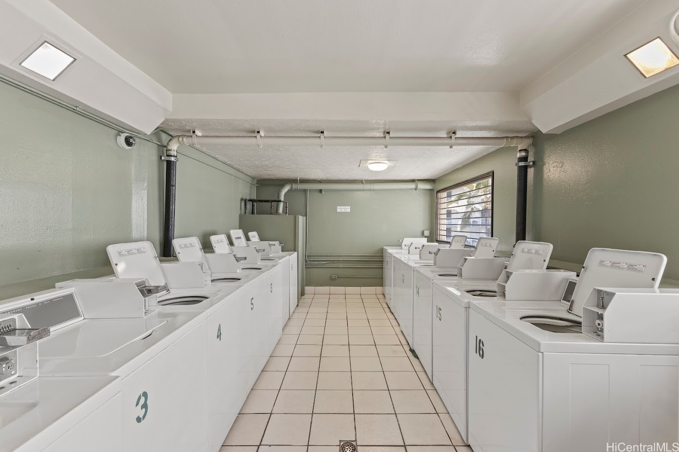 Communal laundry room with rows of white washing machines and tiled floors.