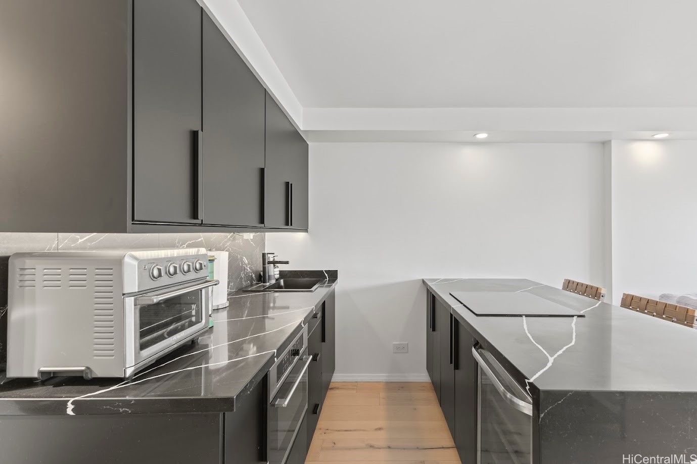 Modern kitchen with dark gray cabinets, veined stone countertops, and a large island.