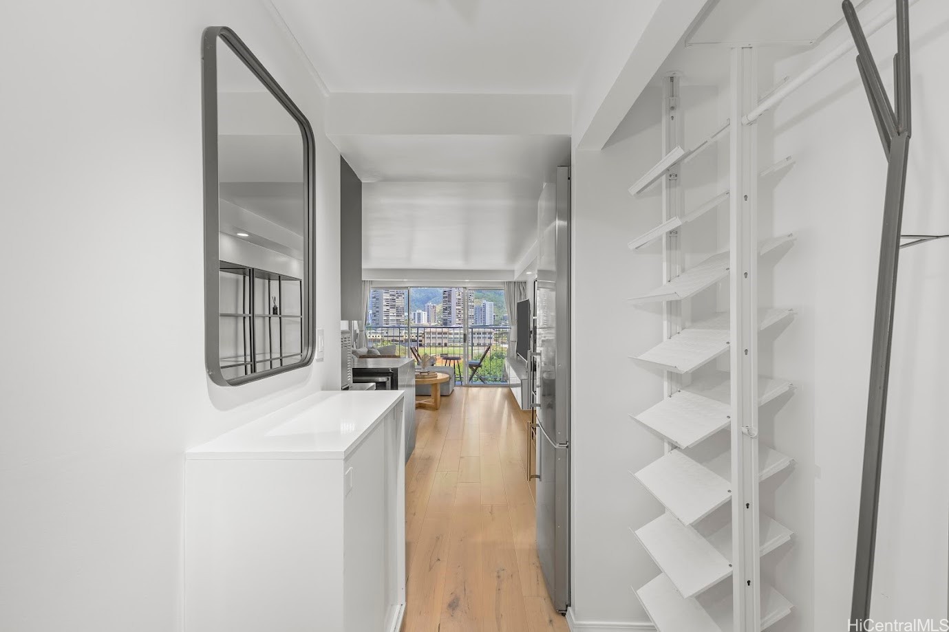 Condo entry hallway with built-in shelving and wood floors, opening to a furnished living area with city views.