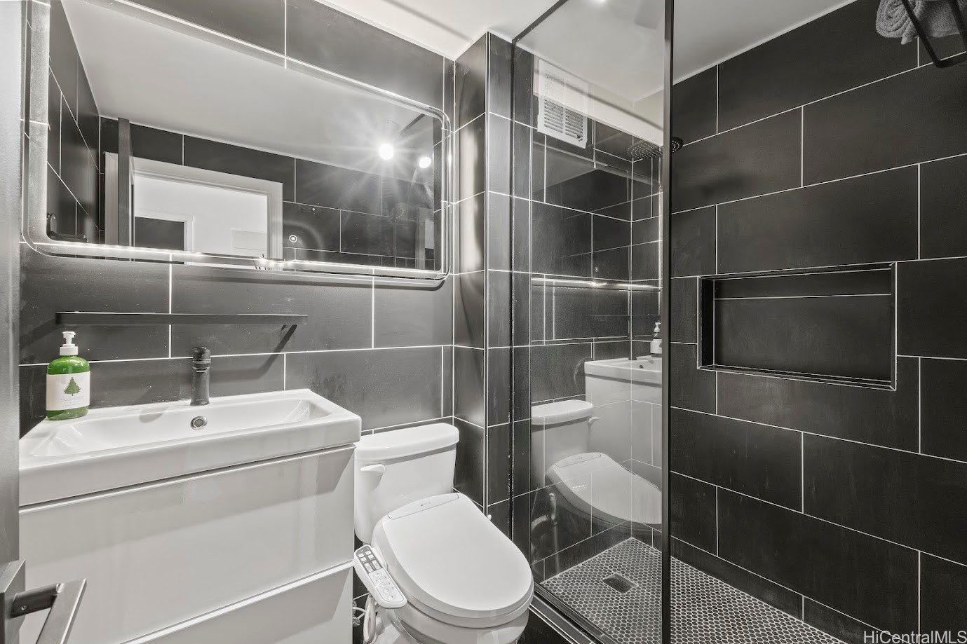 Bathroom with charcoal tile, a glass-enclosed shower, white vanity, and toilet.