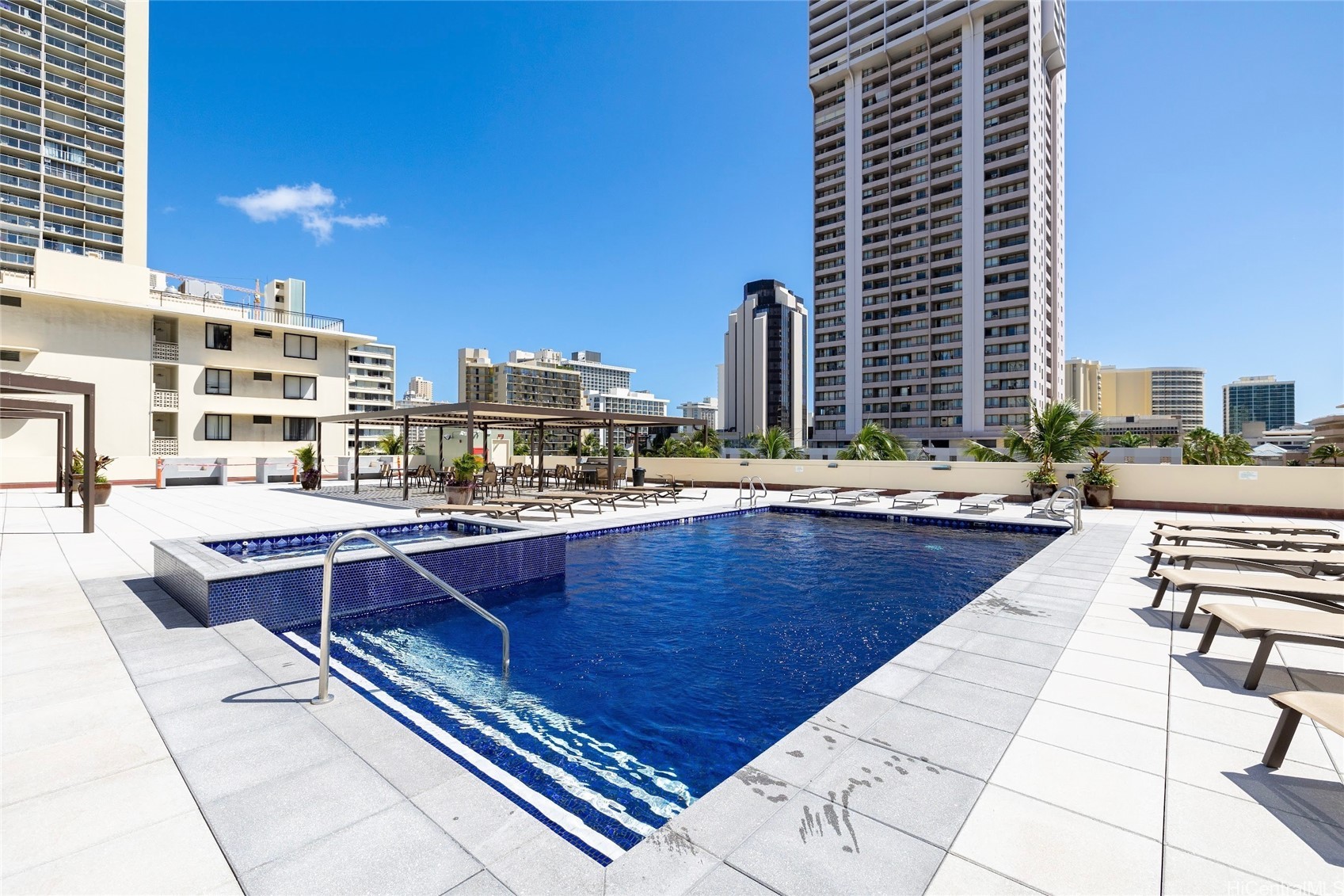 Rooftop swimming pool and spa surrounded by lounge chairs, with Honolulu high-rises in the background.