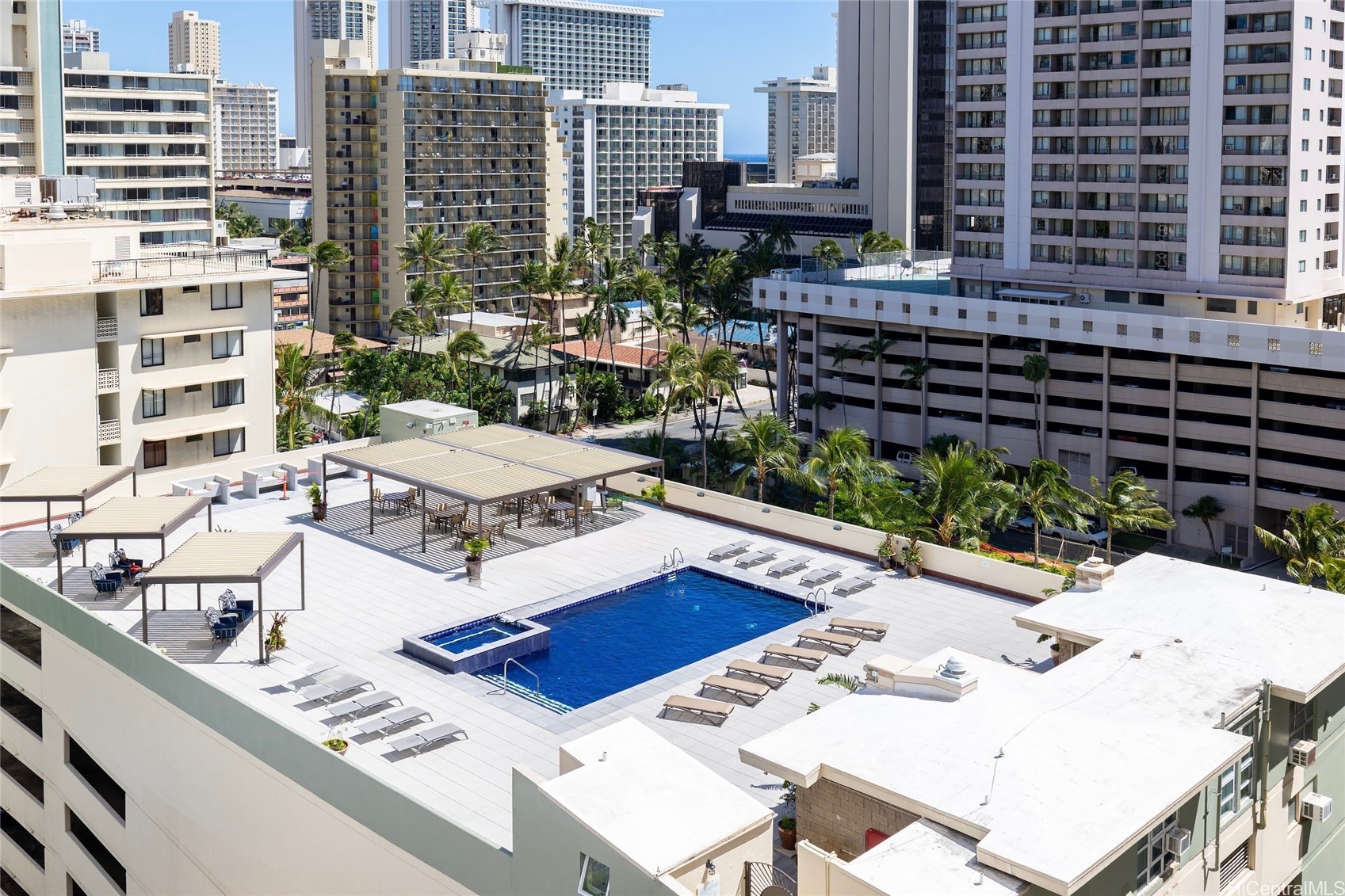 Condominium pool deck with a blue swimming pool, hot tub, lounge chairs, and shaded pergolas.