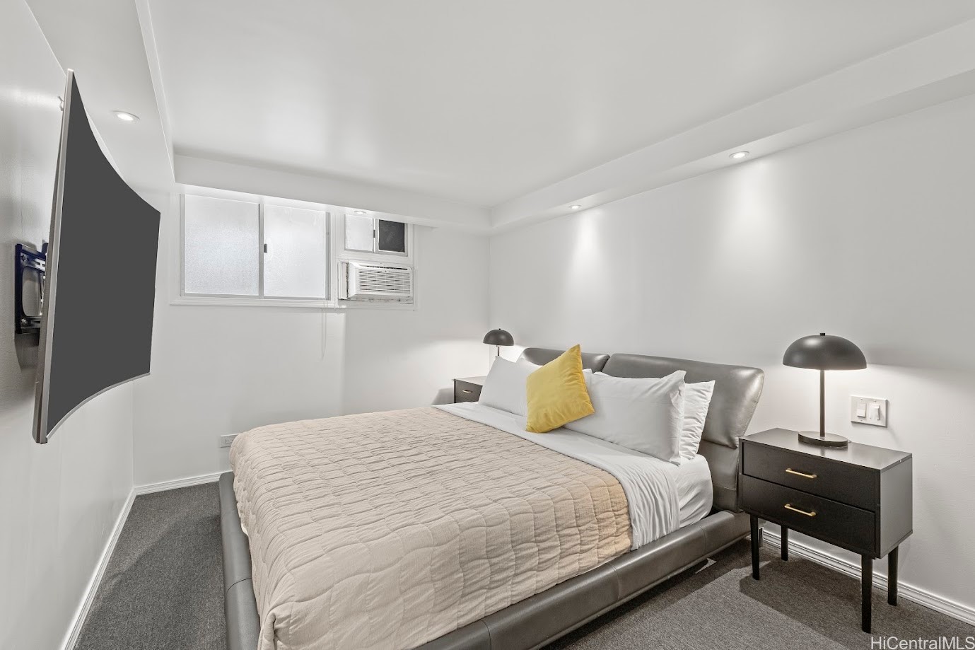 Bedroom with a gray upholstered bed, yellow accent pillow, and wall-mounted television.
