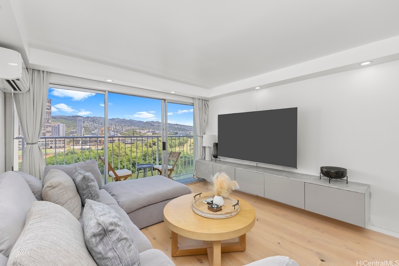 Living room with a gray sectional, balcony doors, and views of Honolulu’s buildings and mountains.