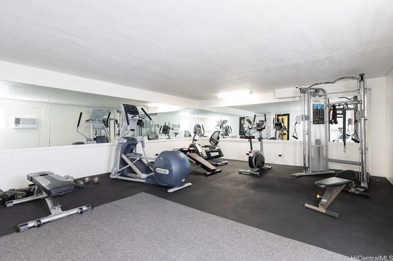 Fitness room with mirrored walls, cardio machines, weight benches, and a cable machine.