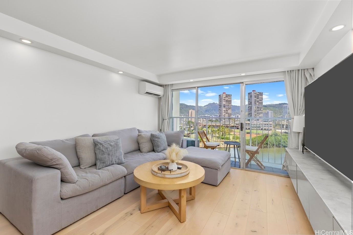 Living room with a gray sectional and balcony views of Honolulu high-rises and mountains.