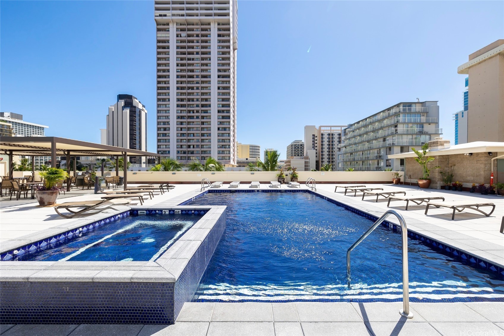 Rooftop swimming pool and hot tub surrounded by loungers, with Honolulu high-rises in the background.