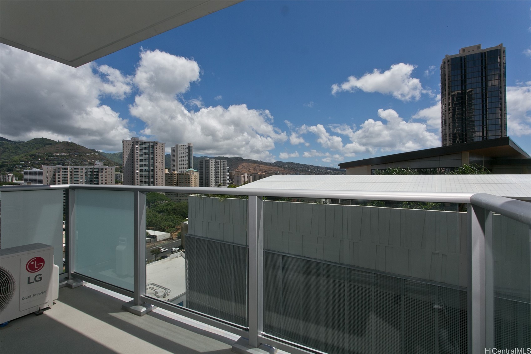 Balcony with glass railing overlooking Honolulu high-rises and green hills.