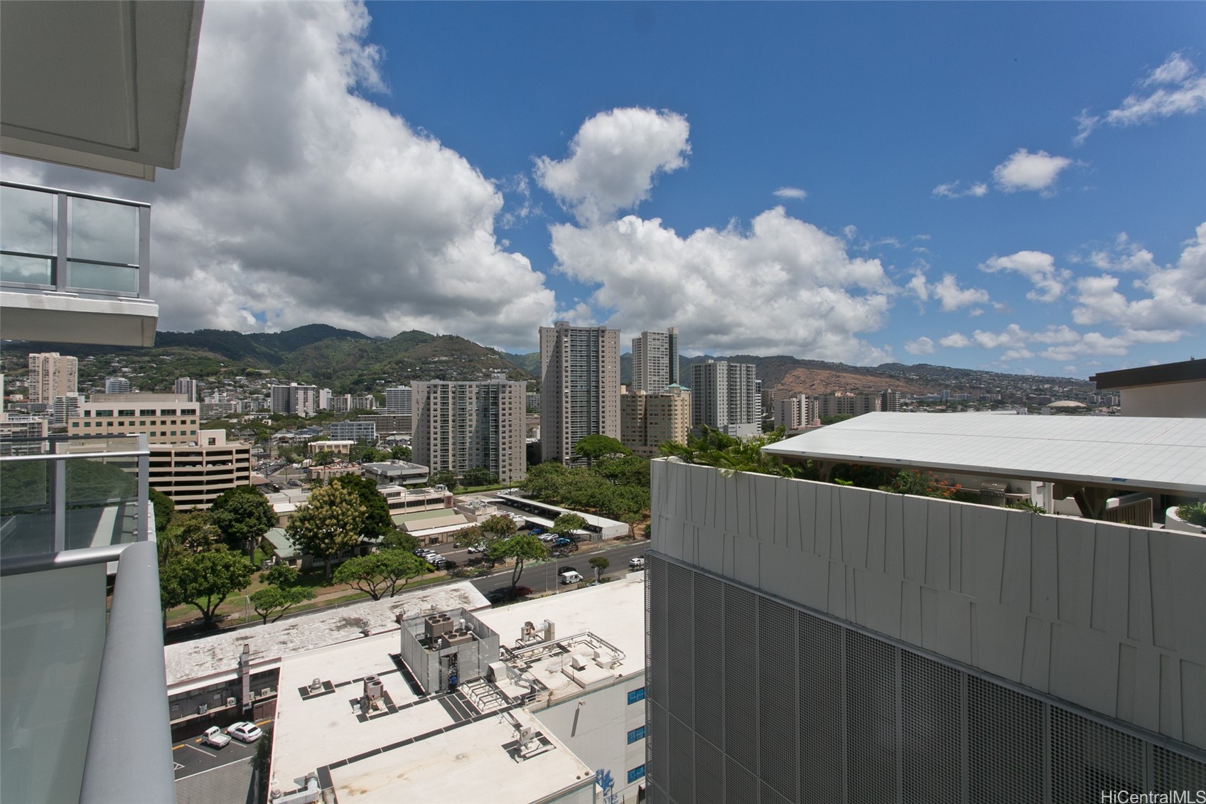 Honolulu city and mountain view from a high-rise balcony, framed by neighboring buildings.