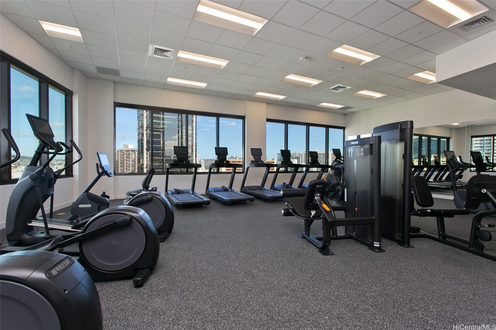 Fitness center with cardio and weight machines and large windows overlooking the city.