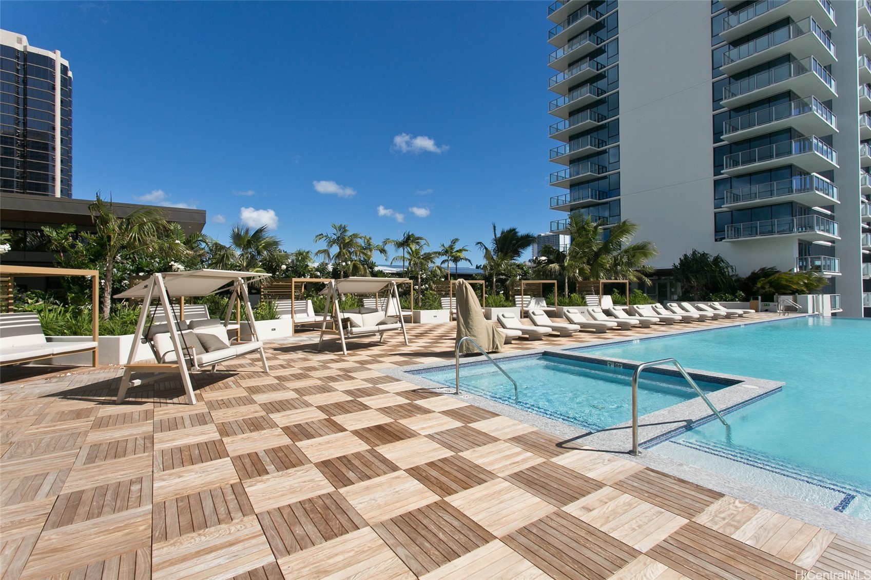 Condominium pool and sun deck with timber decking, lounge chairs, and cabanas.