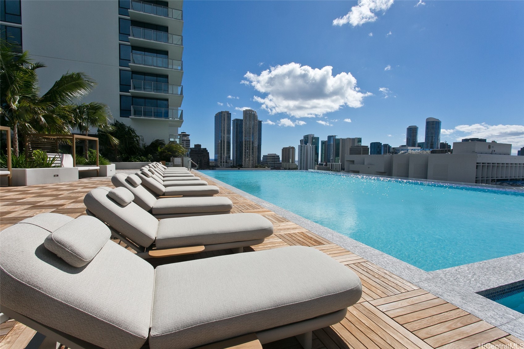 Rooftop pool with cushioned loungers and Honolulu high-rises in the background.