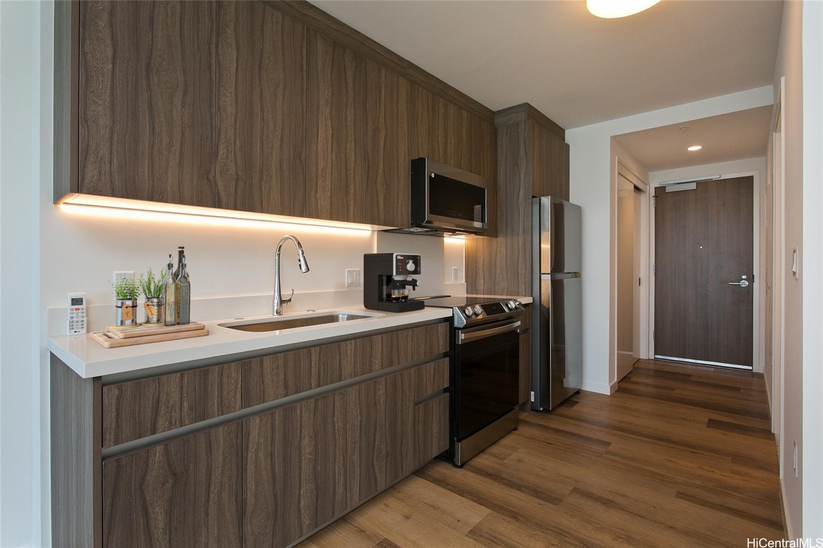 Modern kitchen with dark wood cabinetry, white counters, and stainless steel appliances.