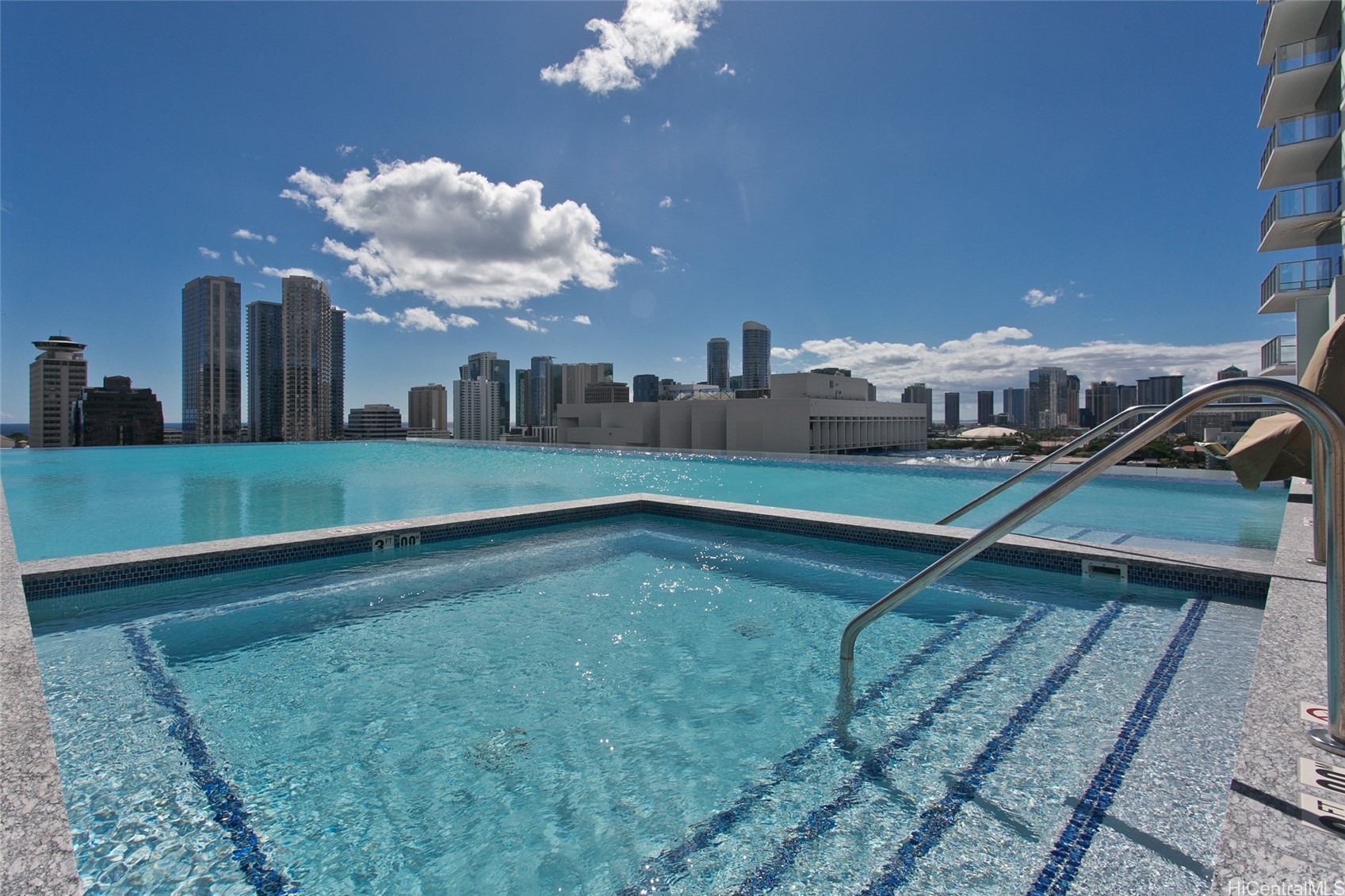 Rooftop pool with submerged steps and handrail overlooking Honolulu’s high-rise skyline.