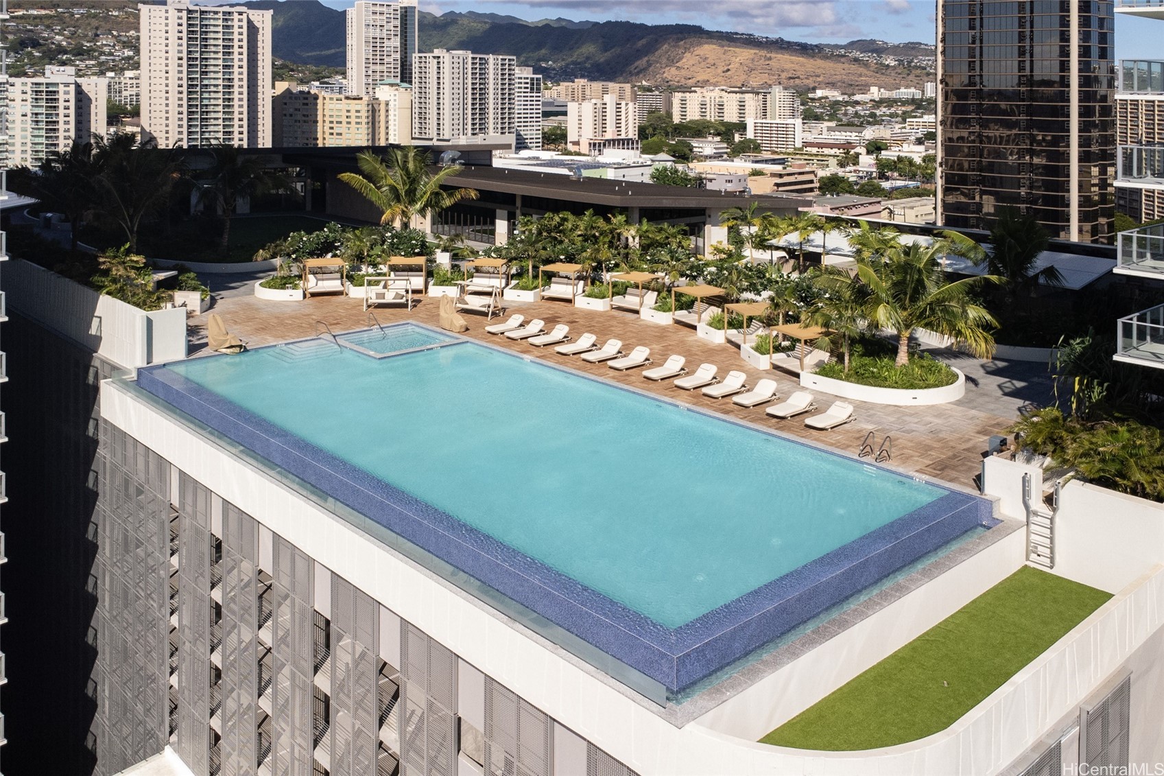 Rooftop pool and sun deck with lounge chairs, overlooking Honolulu buildings and mountains.