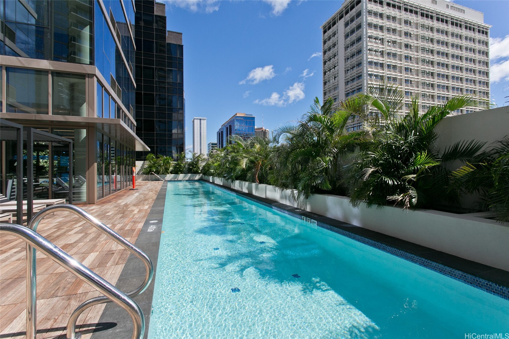 High-rise condominium pool with a tiled deck, palm landscaping, and city buildings.