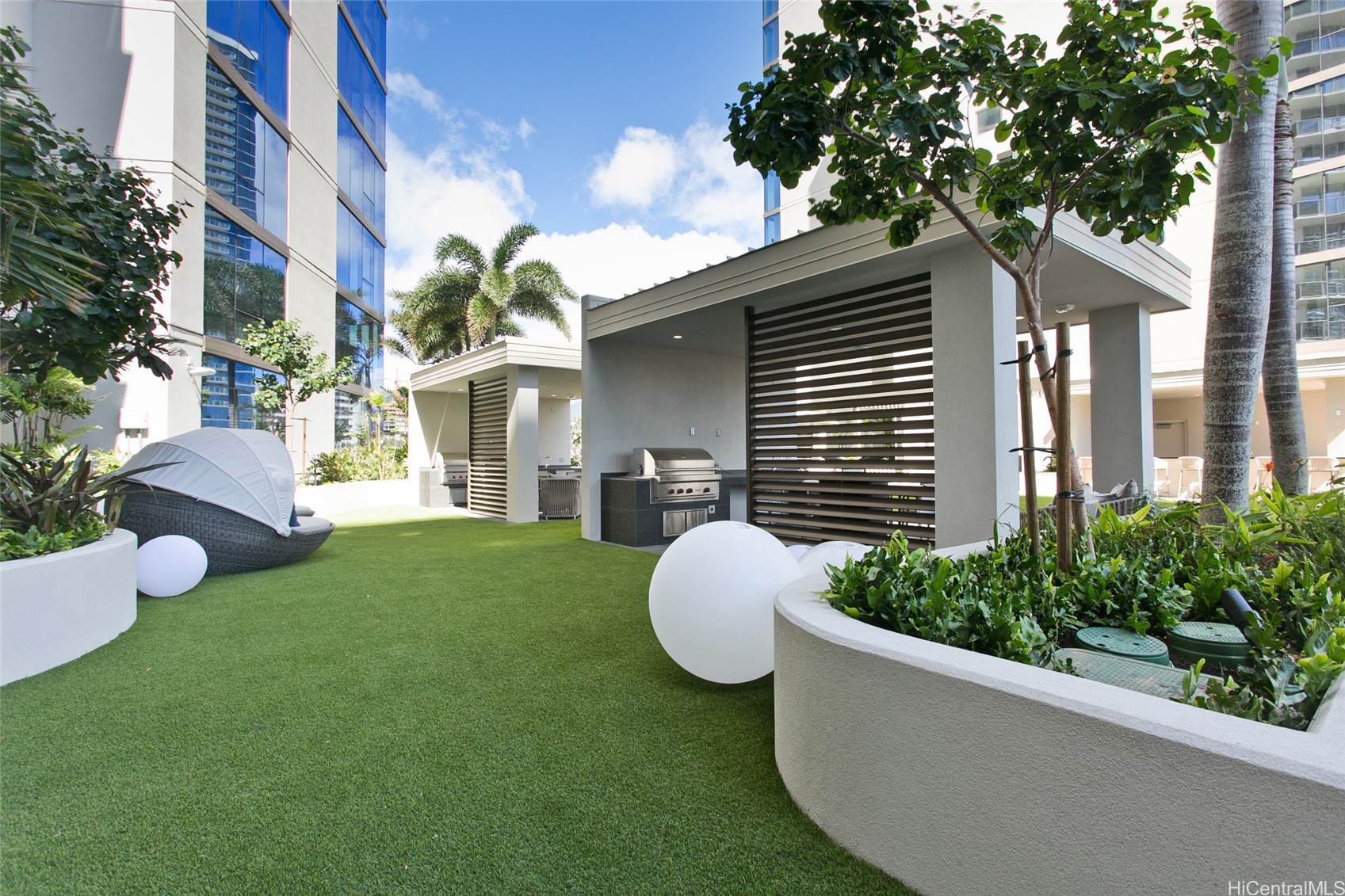 Outdoor courtyard with covered barbecue stations, artificial turf, and modern seating between high-rise buildings.