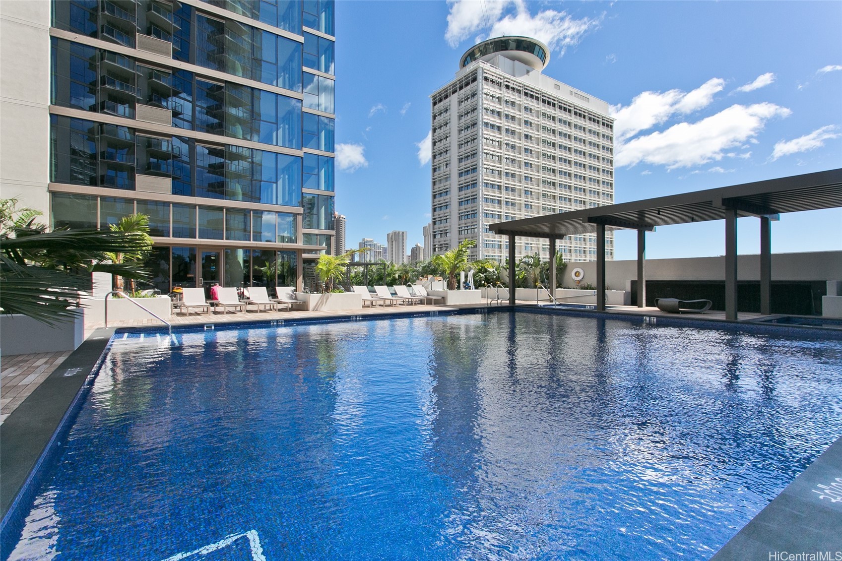 Rooftop swimming pool with lounge chairs, pergola, and Honolulu high-rises.