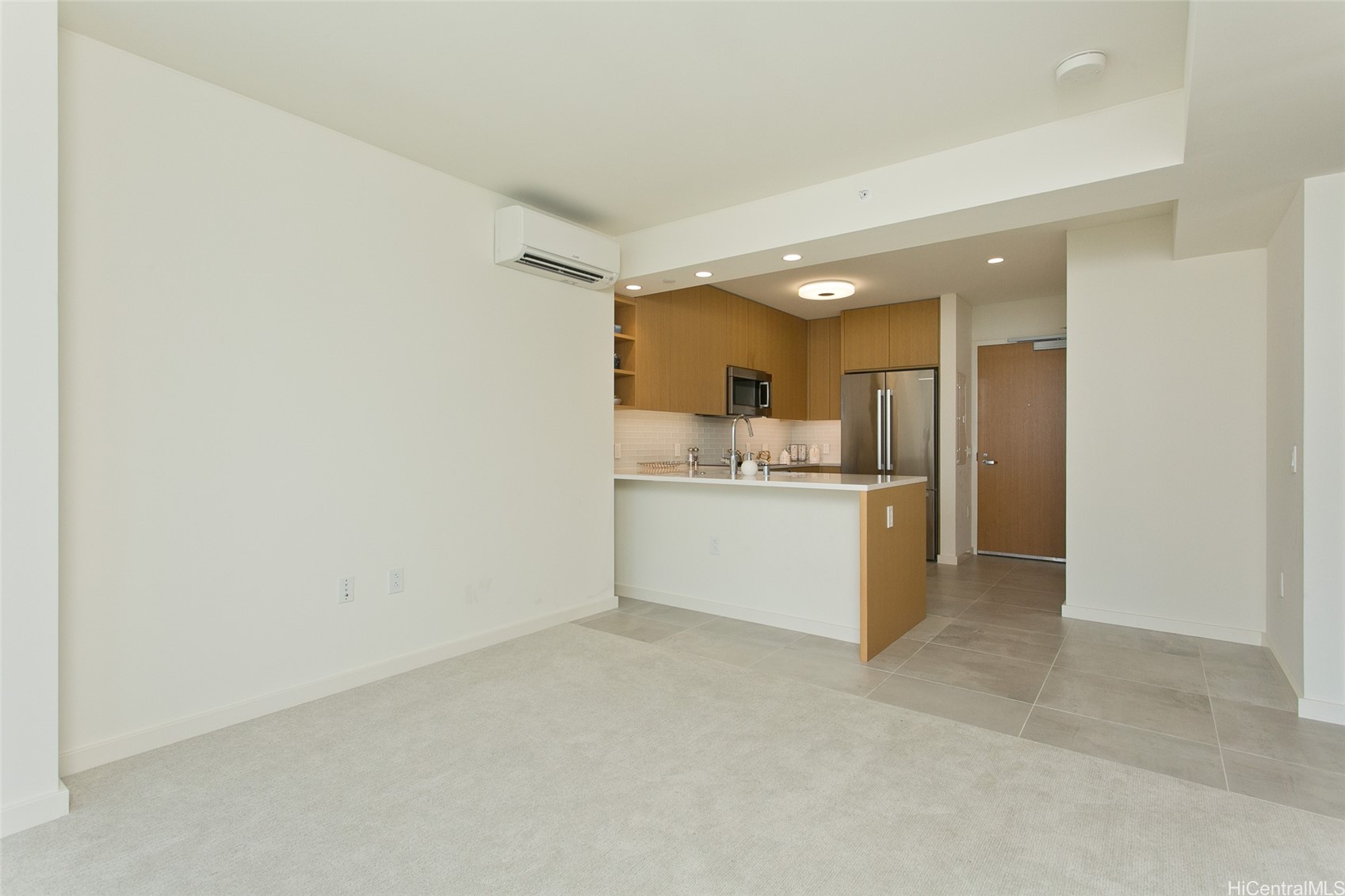 Unfurnished living area opening to a kitchen with wood cabinets, breakfast bar, and stainless steel appliances.
