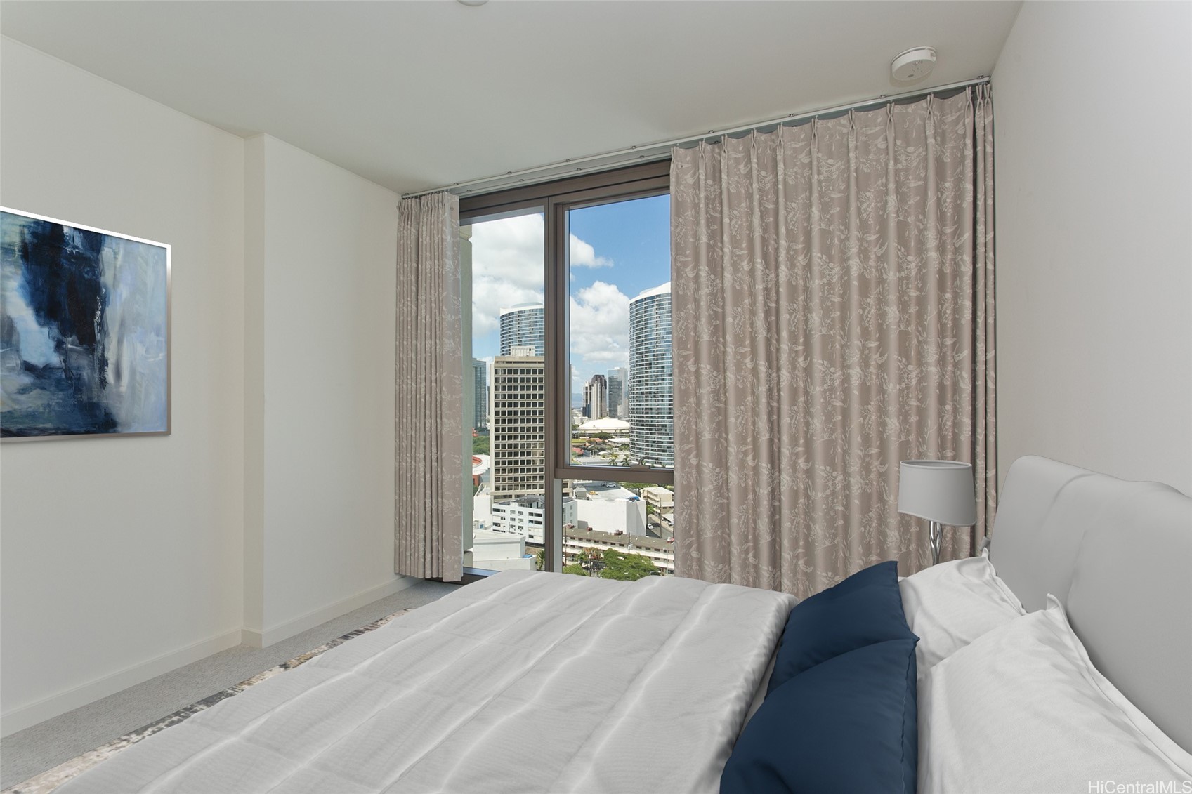 Furnished bedroom with navy pillows and a large window overlooking Honolulu high-rises.