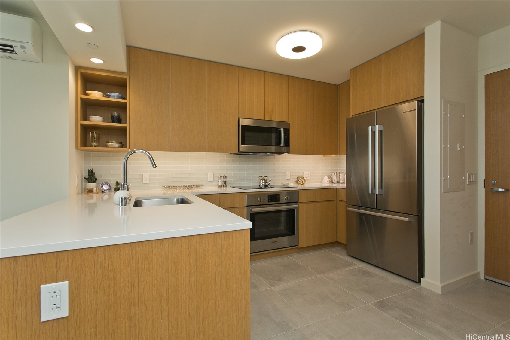 Modern kitchen with warm wood cabinets, white peninsula, and stainless steel appliances.